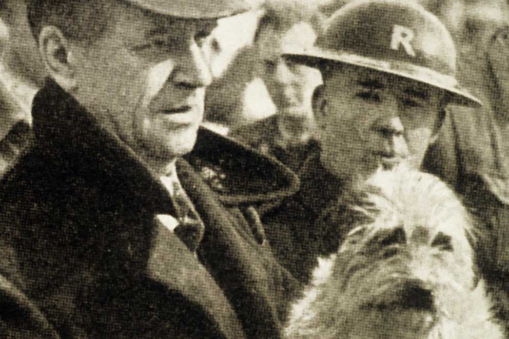 An old black and white image of two male RSPCA inspectors, one holding a scruffy mixed breed dog.