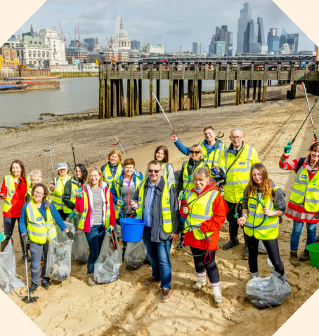 Several people on a beach in hi vis jackets litter picking.