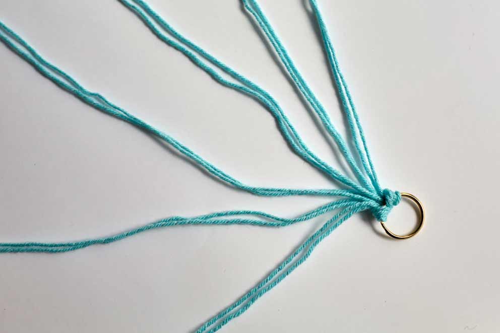 Twelve strands of turquoise wool attached to a metal keyring, fanned out neatly on a white surface. Each pair of strands is tied through the ring using a lark’s head knot.